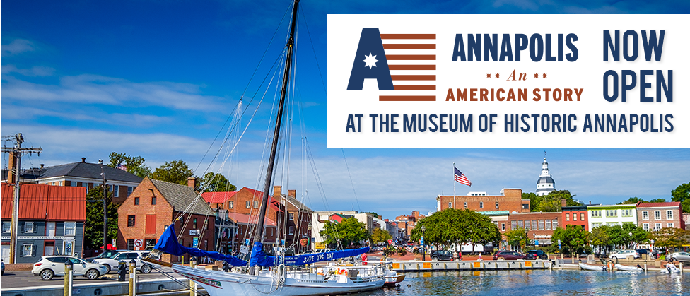 The water and dock in the Annapolis Harbor, a boat with a blue sail that reads Save The Bay in the foreground, with brick buildings lining the street in the background. The white dome of the Maryland State House and an American flag are visible in the background against a blue sky with wispy white clouds.