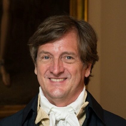 A headshot of a man with a white ascot and black coat