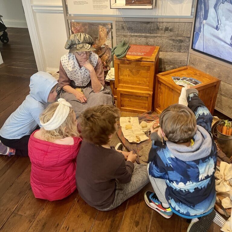 A woman in period dress shares about history with a group of young children