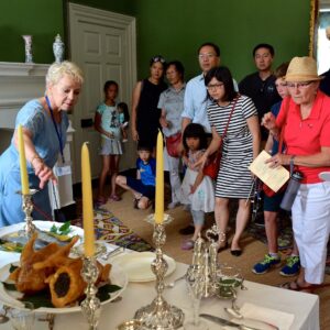 A museum docent shares a dining table display of food and serveware to a group of people.