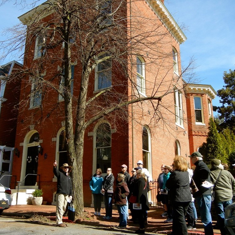 A guide leads a group on a walking tour in front of a brick home.