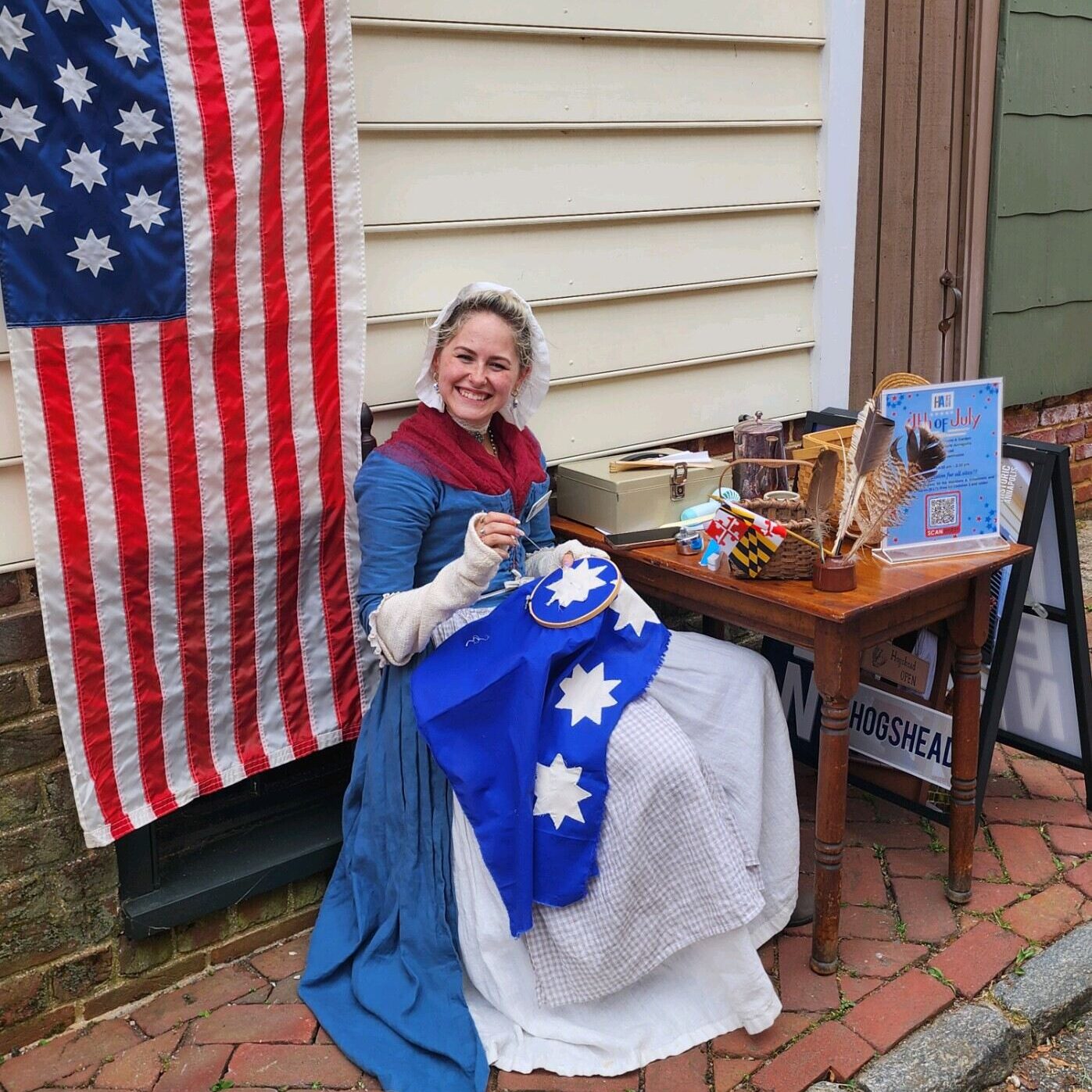 A young women in colonial dress sews a flag