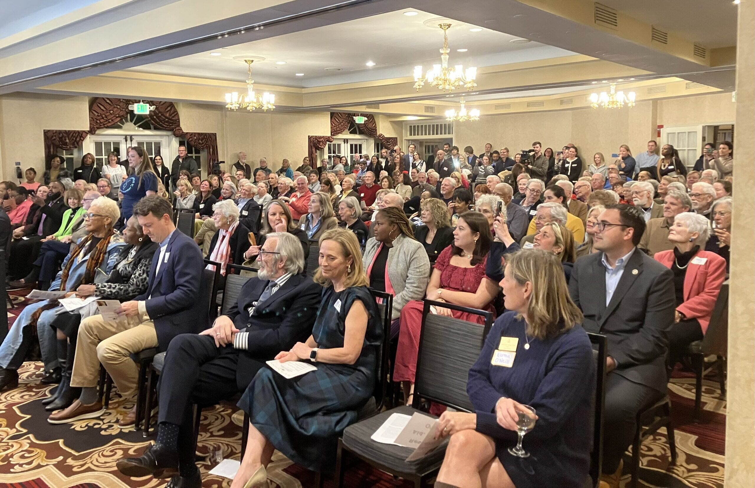 A group of people sit in a ballroom.