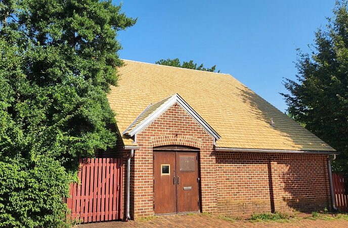 A brick building with a cedar shingle roof and a red fence.