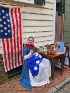 Carlea West in colonial dress sewing a flag