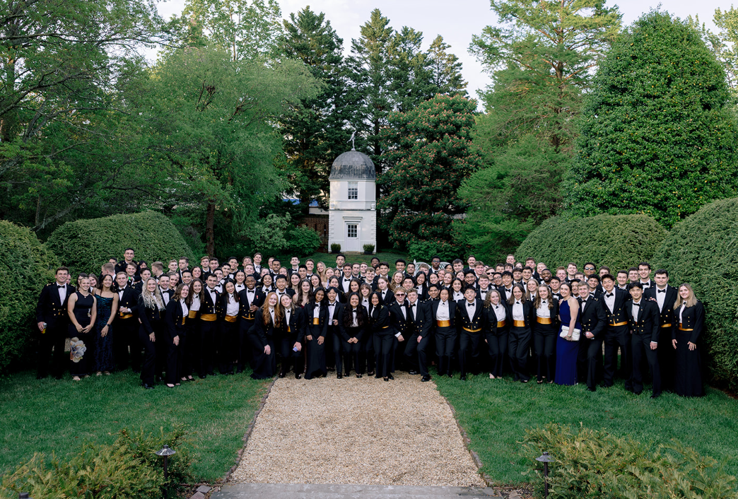 A company of USNA Midshipmen in formal attire in a colonial garden